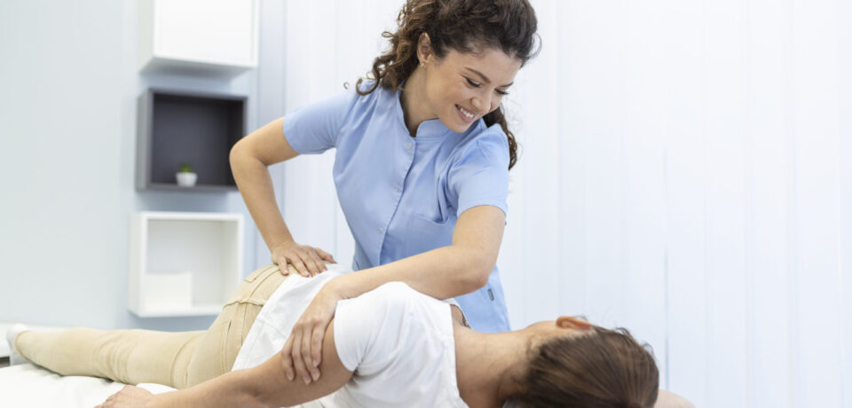 Young woman doctor chiropractor or osteopath fixing lying womans back with hands movements during visit in manual therapy clinic. Professional chiropractor during work Acute and Chronic Lower Back Physiotherapy